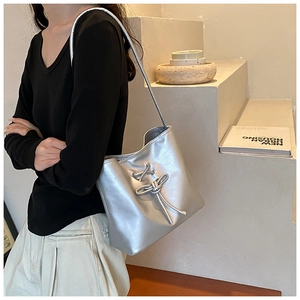 Detail of silver metallic shoulder bag with lace-up bow detail worn by a model