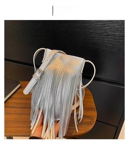 Detailed view of silver crossbody bag featuring long metallic tassels and adjustable strap
