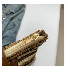 Close-up detail of golden metal zipper and striped texture on straw woven tote bag