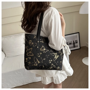 Detail of black tote bag featuring golden butterfly patterns and long shoulder straps