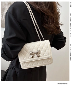 Macro view of white quilted shoulder bag featuring a decorative silver metal bow clasp