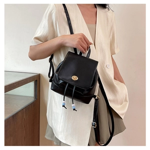 Close-up of mini black leather backpack featuring gold twist lock and beaded drawstring details