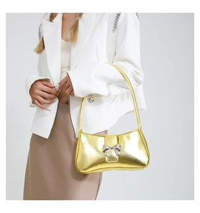 Metallische goldene Schultertasche mit silberner Schleife getragen von einem Model
