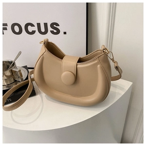 Detail view of a beige minimalist hobo bag with a large covered buckle on a geometric stand