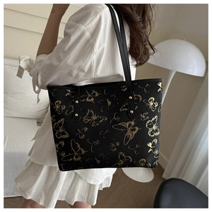 Detail of black leather tote bag with gold butterfly embroidery and sturdy metal rivets
