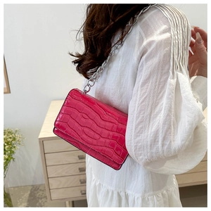 Detail of fuchsia crocodile texture crossbody bag with silver chain on white dress