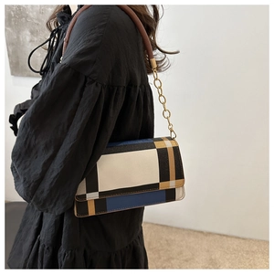 Detail of color-block shoulder bag featuring a metal chain strap against a black skirt