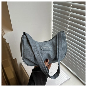 Detail view of grey denim hobo bag featuring a round leather fashion logo and wide strap