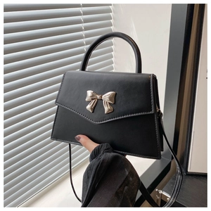 Detail of elegant black crossbody bag with gold bow clasp and smooth matte leather finish