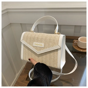 Détail du sac en paille tissée avec bordure en cuir blanc et plaque logo en métal