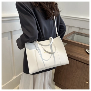 Detail of white faux leather tote bag showing spacious front pocket and gold logo accents