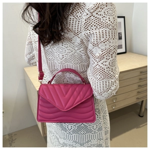 Detail of fuchsia pleated crossbody bag with V-quilted texture worn over white lace dress
