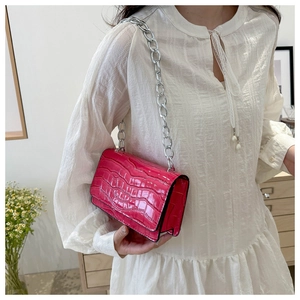 Detail of rose pink crocodile embossed crossbody bag with silver chain on model