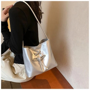 Detailed side view of silver metallic shoulder bag with bow drawstring and glossy finish