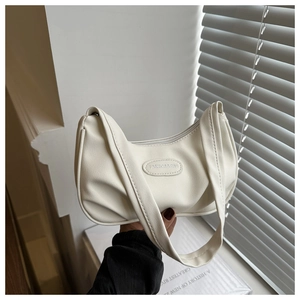 Close-up of beige ruched shoulder bag featuring an oval fashion logo and textured faux leather