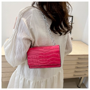 Close-up of fuchsia crocodile pattern crossbody bag with silver chain on model