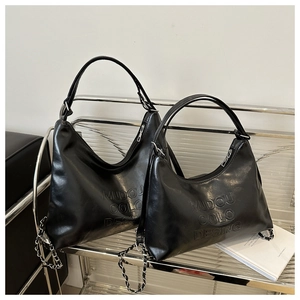 Detail of black leather tote bag with embossed lettering and metal chain strap on shelf