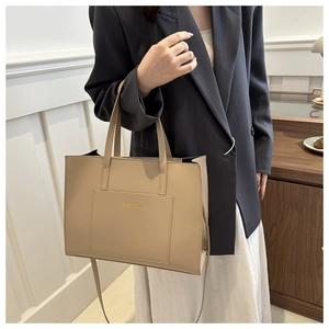 Detailed view of beige tote bag with front pocket and gold logo on a model