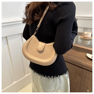 Detail of a beige crescent shoulder bag with a unique round buckle and adjustable strap