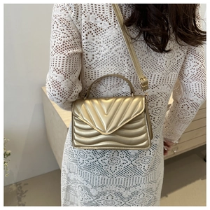 Detail of gold quilted crossbody bag featuring V-shaped stitching and adjustable strap