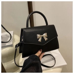 Close-up of black leather handbag featuring a polished silver bow clasp and top handle