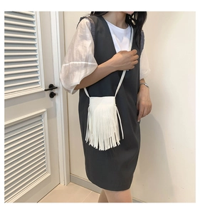 Detail of a white tassel crossbody bag showing long fringes and thin leather strap