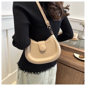 Detail view of beige half-moon shoulder bag with large circular buckle on a model
