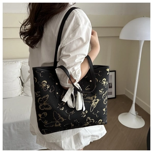 Detail of black tote bag with gold butterfly prints and white ribbon on the shoulder strap