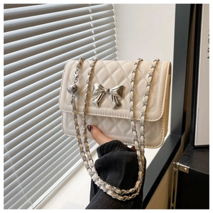 Detail of cream quilted crossbody bag with silver metal bow and chain strap