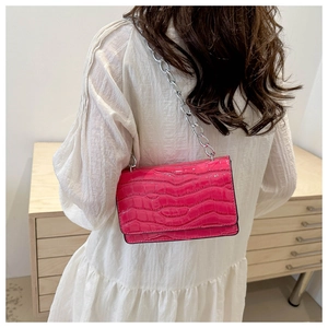 Close-up of bright pink faux leather crossbody bag with crocodile texture and silver chain