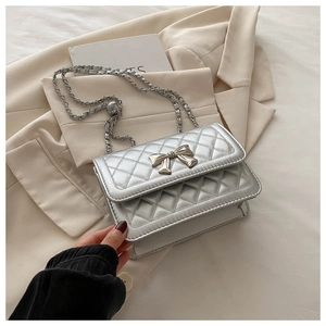 Close-up of silver quilted crossbody bag featuring a metallic bow buckle and chain strap