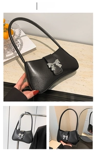 Detailansicht der schwarzen Schultertasche mit silberner Schleifenschnalle und Glanzoptik