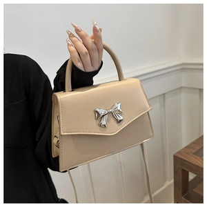 Detailed view of silver bow-knot metal clasp on a beige faux leather handbag