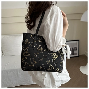 Detail of black tote bag with gold butterfly prints and white bow ribbon on a shoulder