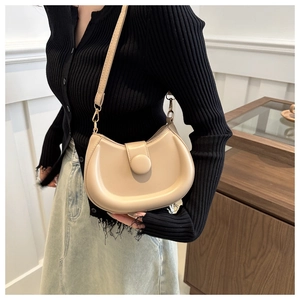 Detail of a beige half-moon shoulder bag featuring a round magnetic buckle and gold hardware