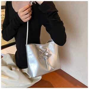 Close-up of metallic silver bucket bag with a bow detail on a stylish model