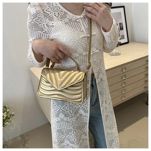 Detail of gold quilted shoulder bag with V-shaped stitching and metallic chain strap