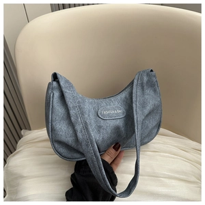 Detail view of crescent shoulder bag featuring grey-blue texture and fashion badge