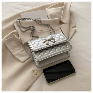 Detail of silver quilted shoulder bag with golden bow buckle and woven chain strap