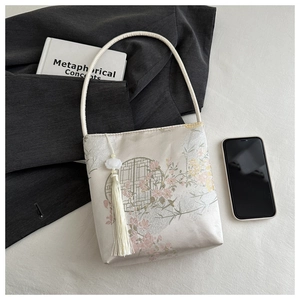 Détail du sac seau en satin de soie avec broderie florale et pompon décoratif blanc