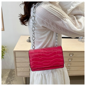 Rose red crocodile embossed crossbody bag with silver chain strap worn by a model