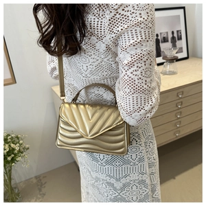 Detail of gold V-quilted faux leather crossbody bag with top handle and metal finish