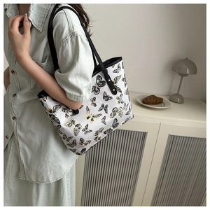Detail of white tote bag with butterfly print and black handles with gold rivets