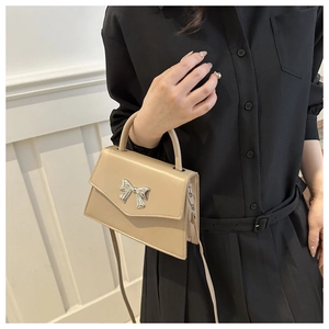 Detail of beige square handbag featuring a silver metal bow buckle and smooth leather