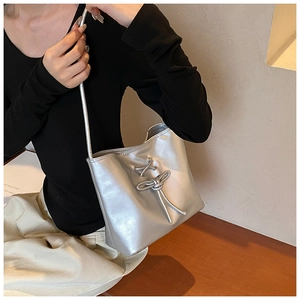 Detail of silver shoulder bag with metallic texture and 3D knot design on the model