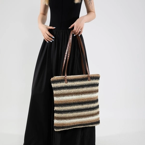 Large striped straw tote bag with brown leather straps worn by model on black dress