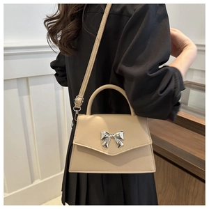 Detail of elegant beige crossbody bag with silver bow clasp and adjustable strap