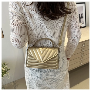 Detail of gold quilted crossbody bag with metal ring handle and textured V-stitch design
