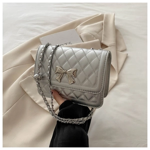 Detail of silver quilted shoulder bag with bow and adjustable chain on beige blazer
