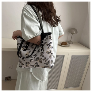 Detail of butterfly print tote bag with black straps and metal rivets in lifestyle setting